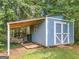 A blue shed with a covered area, located in a wooded area, great for storage at 1041 Sandy Ridge Rd, Mcdonough, GA 30252
