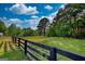 Picturesque view of a green field with a black wooden fence and mature trees under a cloudy sky at 540 Benton Rd, Covington, GA 30014