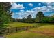 Scenic view of a grassy field with a wooden fence and mature trees under a blue, cloudy sky at 540 Benton Rd, Covington, GA 30014