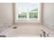 Close-up of a soaking tub with marble-look tile surround and a window at 61 Main St, Moreland, GA 30259
