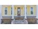 Inviting front porch of a yellow home, featuring a wooden deck, brick steps, and classic white columns at 929 Hilltop Park Ct, Dacula, GA 30019
