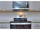 Close-up of modern range and stainless steel microwave with gray cabinets and white tile backsplash at 6214 Ripple Way # 91, South Fulton, GA 30349