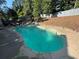 A kidney shaped pool surrounded by concrete has a sun shelf and an umbrella on a patio nearby at 1210 Swan Mill Ct, Suwanee, GA 30024