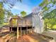 View of the home's back exterior showcasing a wooden deck and lush landscaping, backed by mature trees at 5394 Muirwood Pl, Powder Springs, GA 30127