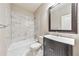 Bathroom featuring a shower-tub combo with marble tiling, dark vanity with sink, and a dark framed mirror at 2423 Rosapenna Nw Ln, Kennesaw, GA 30152