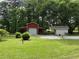 A red barn-like structure with a roll-up door and a beige outbuilding are situated on a grassy lot with mature trees at 6054 Nebo Rd, Hiram, GA 30141