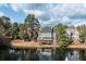 Scenic view of a lakeside home with a fountain and mature trees on a sunny day at 6191 Talmadge Run, Acworth, GA 30101