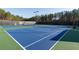 Up close, the vibrant blue tennis court is surrounded by dark fencing and tall pines at 6191 Talmadge Run, Acworth, GA 30101