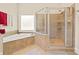 Bathroom with a glass-enclosed shower and a soaking tub by a window, tiled in neutral earth tones at 3420 Aviary Ln, Acworth, GA 30101