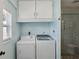 Bright laundry room with white washer, dryer, upper cabinets, and tiled shower at 1522 Waltham Se Pl, Atlanta, GA 30316