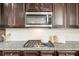 Close up of a stainless microwave and a gas cooktop on granite counter with dark cabinets at 7710 Tiberon Pkwy, Cumming, GA 30028