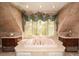 The luxurious bathroom features a pink soaking tub with gold fixtures, surrounded by custom cabinets and a serene window view at 115 Russell Rd, Roswell, GA 30075