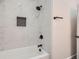 Close-up of sleek white tiled shower and tub with matte black fixtures and a built-in niche at 4322 Timberland Sw Dr, Lilburn, GA 30047