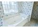 Oval bathtub with window in a floral wallpapered bathroom at 95 Brandon Dr, Covington, GA 30016