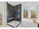 A luxurious bathroom features a glass shower with black herringbone tile and a soaking tub with natural views at 135 Cedarwood Ln, Roswell, GA 30075