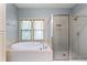 Well-lit bathroom featuring an oval tub, glass-enclosed shower, and a window for natural light at 9032 Selborne Ln, Chattahoochee Hills, GA 30268