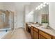 Spacious bathroom featuring double vanities, large mirror, neutral tile flooring, and a glass-enclosed shower and tub at 535 Cape Ivey Dr, Dacula, GA 30019