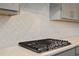 Detailed view of a modern gas cooktop, set against a white, decorative backsplash in a gray kitchen at 6935 Melody Dr, Buford, GA 30518