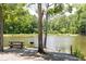 Scenic pond view with a picnic bench and grill on the shore, surrounded by mature trees and foliage at 512 Altamaha Ct, Locust Grove, GA 30248