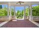 Spacious covered patio featuring brick floors, classic columns, and a tranquil view of the lush garden beyond at 5200 Moore Rd, Suwanee, GA 30024