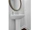 Bathroom with white pedestal sink, round mirror and dark hardwood floors at 1202 Ida Woods Ln, Lawrenceville, GA 30045