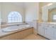 Bathroom featuring a soaking tub under an arched window and a vanity with a large mirror at 3184 Islesworth Trce, Duluth, GA 30097