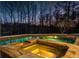 Outdoor pool and hot tub area lit up at night and fenced in with view of the woods at 500 Covington Cv, Alpharetta, GA 30022