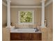 Close-up of tub with brown cabinets, a garden view, and pillars in an elegant bathroom at 560 Glenmanor Ct, Atlanta, GA 30328