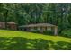 A single story brick home features a large lawn with mature trees and a covered parking area at 6467 Joanna St, Lithia Springs, GA 30122