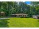 A single story brick home boasts a pristine green lawn, complemented by mature trees and a covered parking area at 6467 Joanna St, Lithia Springs, GA 30122
