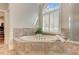 Elegant bathroom with large tub with travertine tile surround and arched window at 4478 Outpost Ct, Roswell, GA 30075