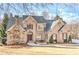 Elegant brick home featuring a stone chimney, arched entry, and lush landscaping at 4478 Outpost Ct, Roswell, GA 30075