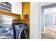 Modern laundry room with front loading washer and dryer, open shelves, and bright yellow accent wall at 1114 Ivey Chase Pl, Dacula, GA 30019