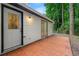 Exterior shot of a white home with a brick patio and a door and sliding glass door, with forest behind at 1428 Muirfield Dr, Stone Mountain, GA 30088