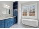 Bright bathroom with a large vanity, blue cabinetry, soaking tub, and a window overlooking the backyard at 5021 Heatherwood Ct, Roswell, GA 30075