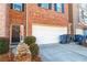 Exterior view of brick townhome with a two car garage, black door, landscaping, and trash cans out front at 1605 Signal Flag Way, Lawrenceville, GA 30043