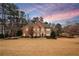 Two-story brick home featuring a manicured lawn and complemented by mature trees under a colorful sunset sky at 5216 Old Mountain Ln, Powder Springs, GA 30127