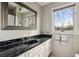 A bathroom with a black marble countertop and a white vanity under a gray-framed mirror near a bright window at 1605 Saint Tropez Way, Atlanta, GA 30350