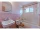 Retro bathroom featuring a tub, sink, toilet, window, and pink brick accent wall at 301 Lady Agatha Ct, Jonesboro, GA 30236