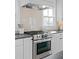 Close up of a stainless steel range oven and exhaust hood with gray tile backsplash and white cabinets at 3326 Springhaven Ave, Hapeville, GA 30354