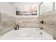 Elegant bathtub with travertine-like tile surround, modern fixtures, and decorative artwork at 613 Everett Ln, Woodstock, GA 30188