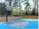 Full-sized basketball court with blue and gray surface surrounded by a retaining wall and mature landscaping at 3553 Old Maple Dr, Johns Creek, GA 30022