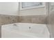 Close up of a white soaking tub with tile surround and chrome fixtures under a window with blinds at 5180 Mirror Lake Dr, Cumming, GA 30028