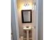 Compact half bathroom featuring a pedestal sink, framed mirror, and updated lighting fixtures at 2403 Brianna Dr, Hampton, GA 30228