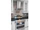Close-up of modern stainless steel range and hood, with glass shelved cabinets at 4830 Rebel Nw Trl, Sandy Springs, GA 30327