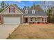 Charming single-Gathering home boasts stone accents, two-car garage, red door and shutters, and landscaped front yard at 10 Oakbrook Ln, Covington, GA 30016