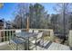 Back deck with dining area, seating and railing, with a view of a lush wooded area and blue sky at 9470 Dominion Way, Alpharetta, GA 30022