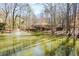 Scenic view of pond with fountain and charming home with wraparound deck in wooded setting at 100 Silverbell Ct, Roswell, GA 30075