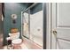 Bathroom featuring a toilet, white tile shower with glass door, and patterned green and white wallpaper at 2595 Ross Rd, Snellville, GA 30039