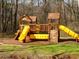 A playground with wooden structures and yellow slides sits among the trees in a common area at 158 Weatherstone Dr, Woodstock, GA 30188